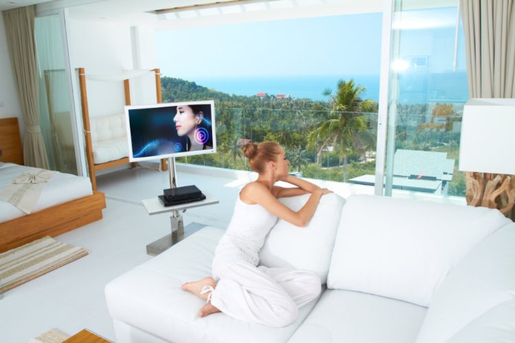 A beautiful woman relaxes on a white sofa in a modern airy bright living-room enjoying the luxury of a tropical lifestyle